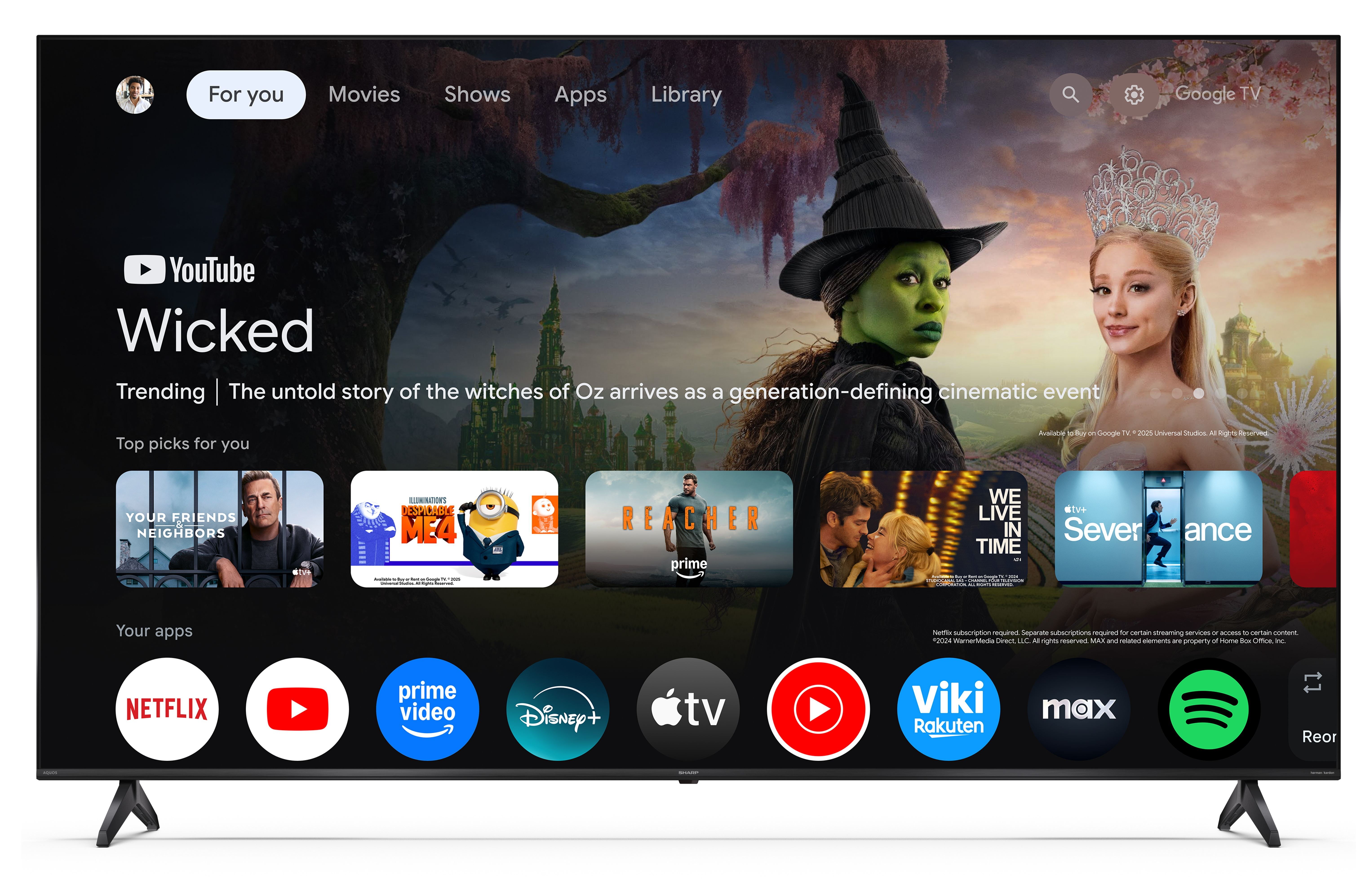 Ekran telewizora wyświetla YouTube, film Wicked i ikony aplikacji. Widoczna jest czarownica i kobieta z koroną.