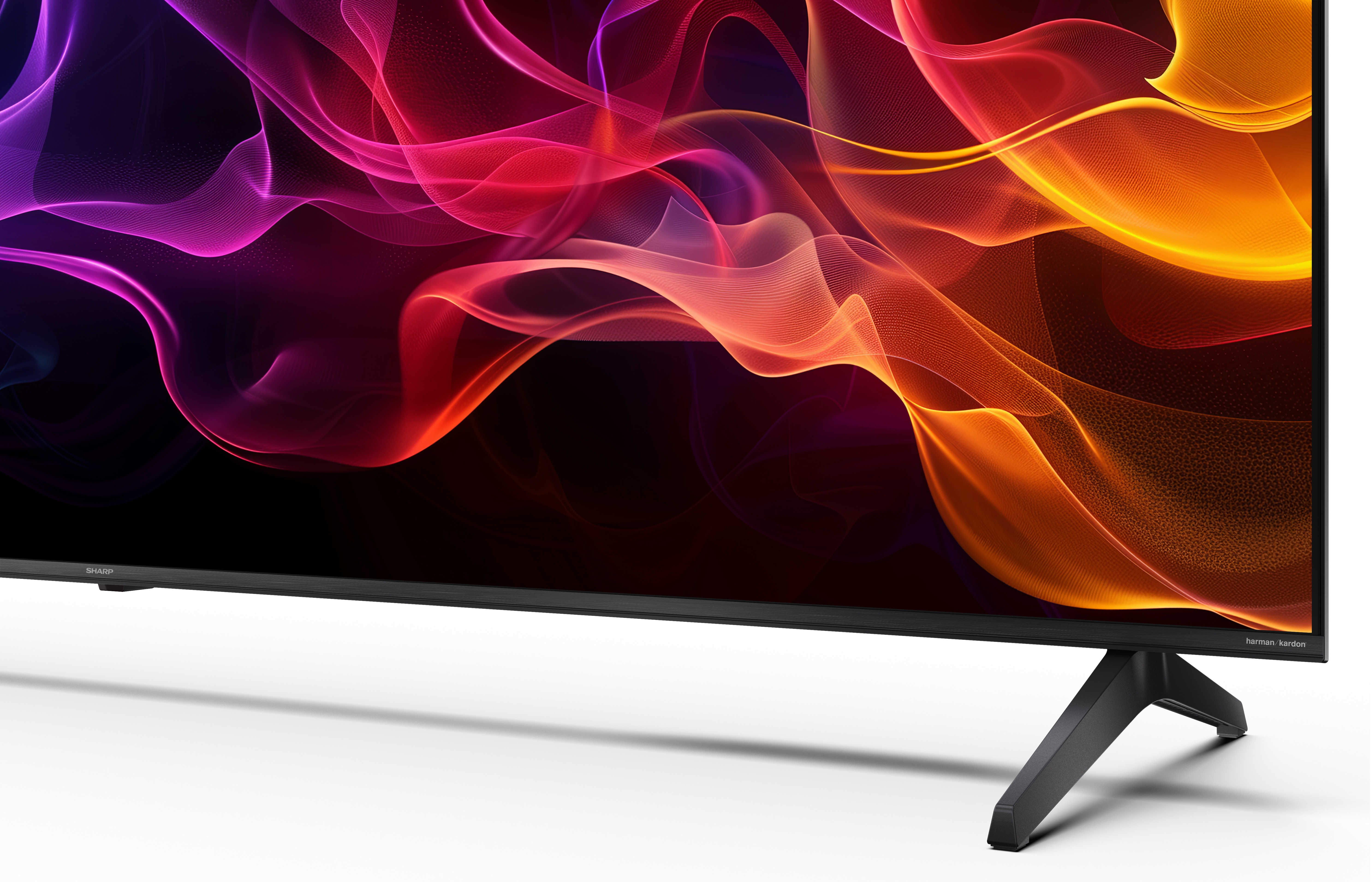 Ekran telewizora wyświetla abstrakcyjne, kolorowe kształty. Czarna ramka i stojak. Białe tło. Logo Harman/Kardon.