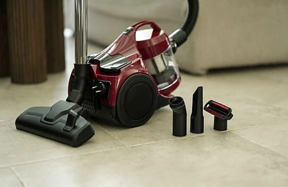 Czerwono-czarny odkurzacz z akcesoriami na kafelkach. W tle sofa i brązowe kolumny.