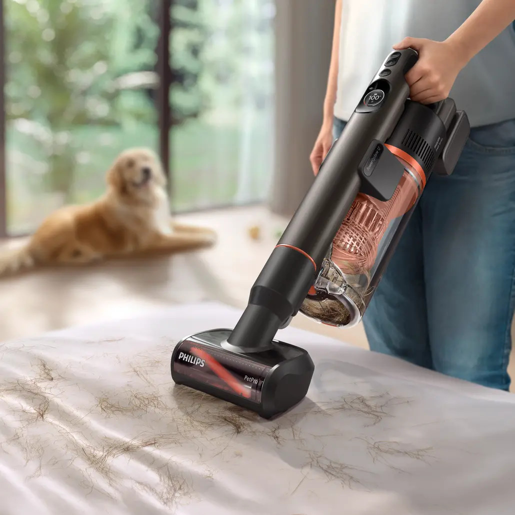 Osoba odkurza łóżko pokryte sierścią zwierząt odkurzaczem Philips. Pies leży w tle.