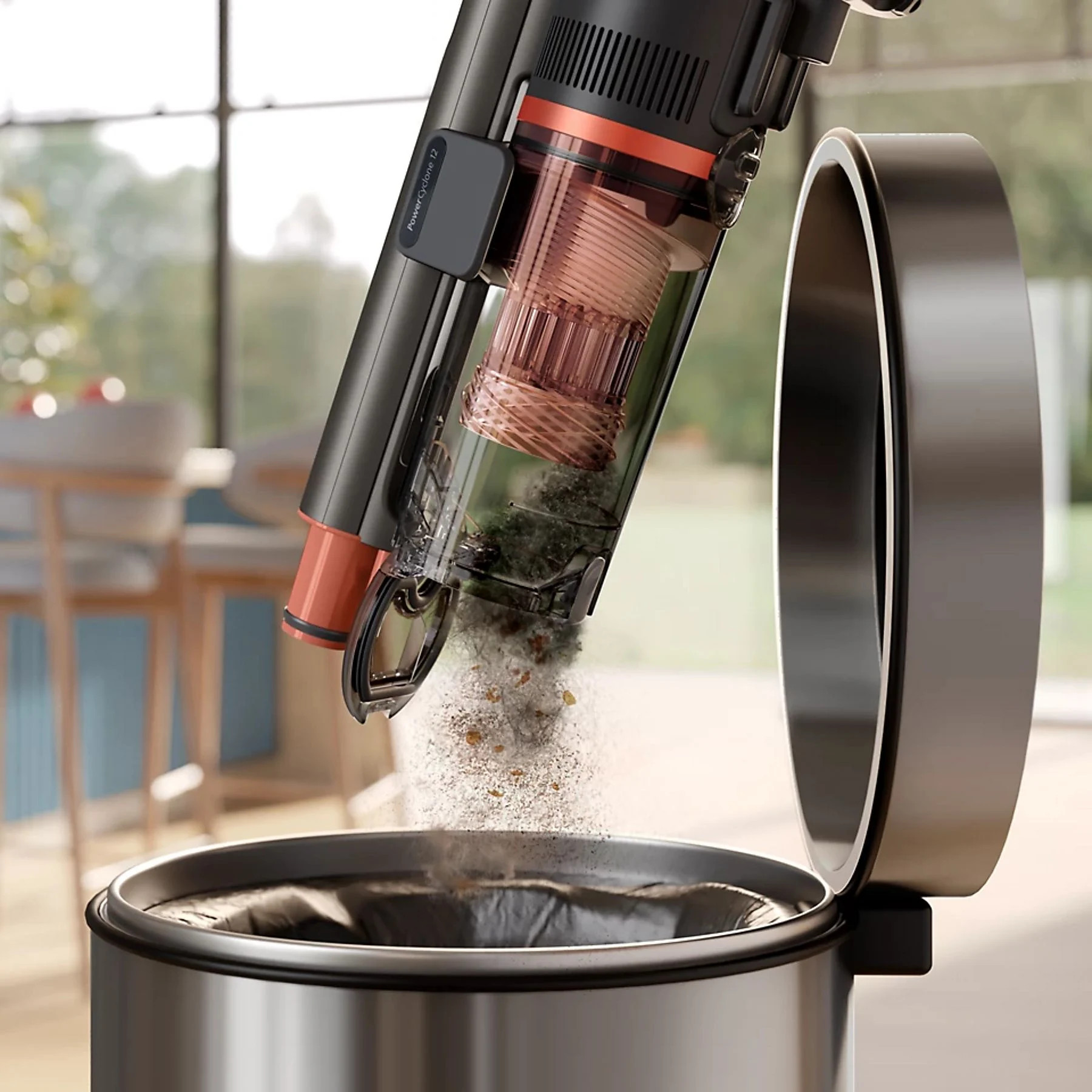 Odkurzacz bezprzewodowy opróżniający zanieczyszczenia do kosza. Odkurzacz jest czarno-pomarańczowy. Kosz jest ze stali nierdzewnej.