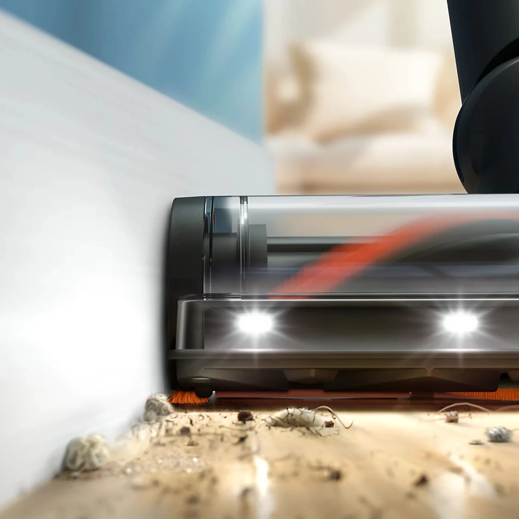 Głowica odkurzacza czyści drewnianą podłogę obok białej ściany. Na podłodze leżą zanieczyszczenia.