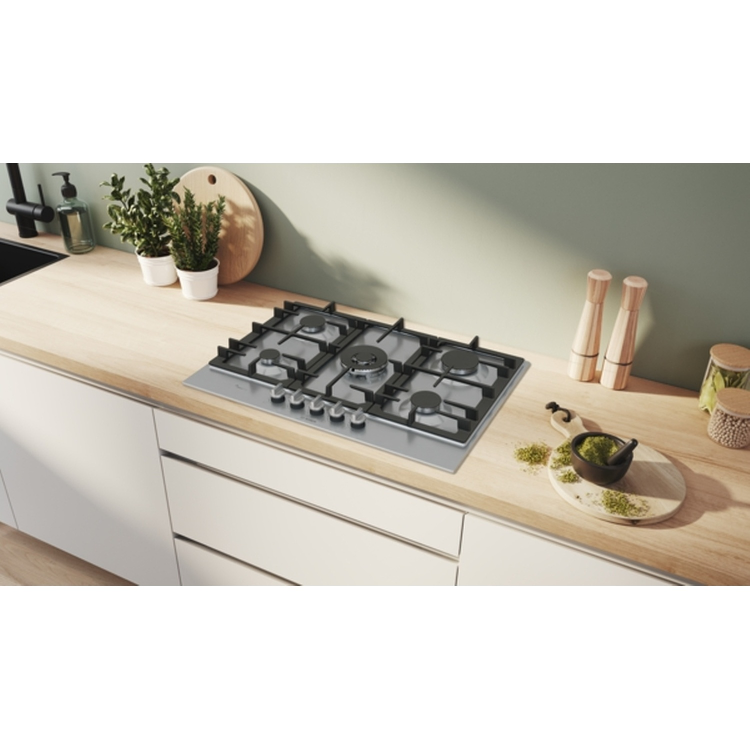 Keuken met gasfornuis, planten, snijplanken en kruiden op een houten aanrecht. Witte kasten eronder.