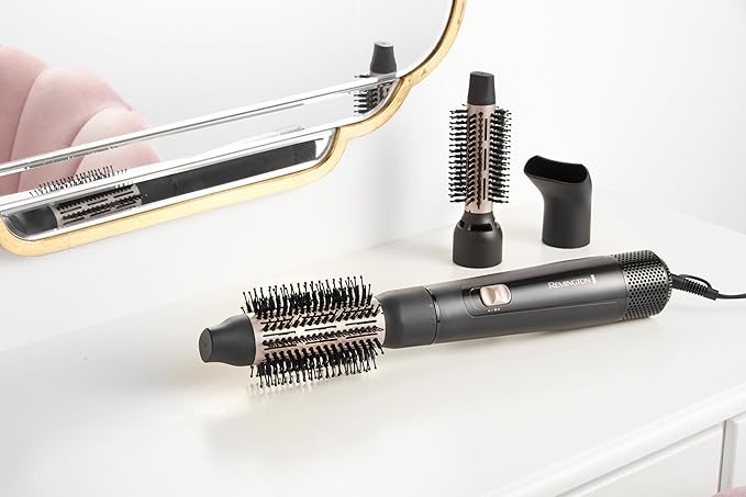 Beyaz bir yüzey üzerinde fırça, kurutucu ve ayna içeren bir saç şekillendirme seti. Remington markası görünür.