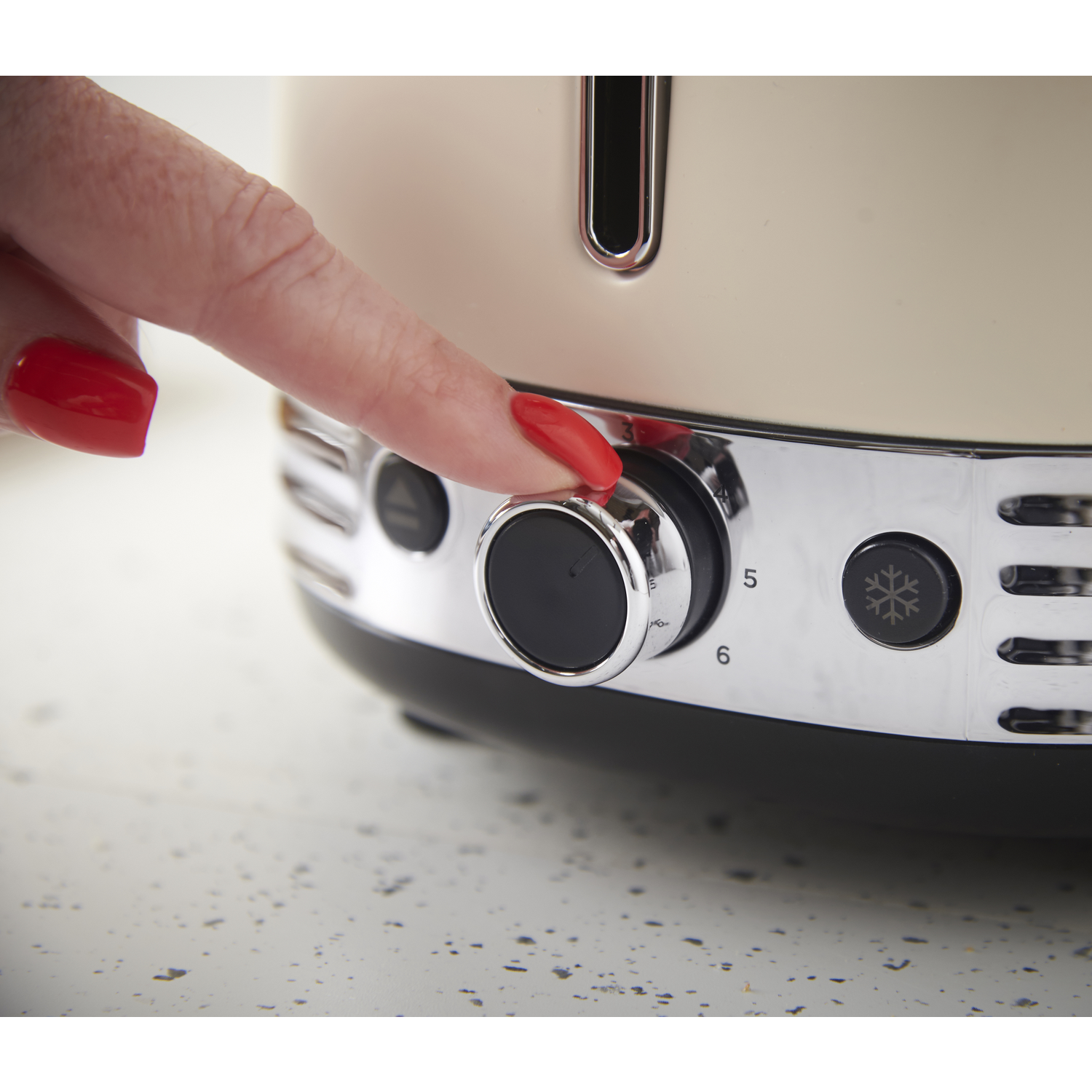 A hand with red nail polish is turning the dial on a cream-colored toaster. The dial is set to 5.
