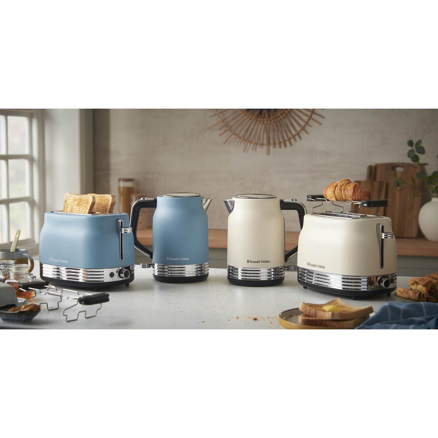 Four Russell Hobbs appliances, including toasters and kettles, are displayed on a countertop. One toaster has bread, another has croissants.