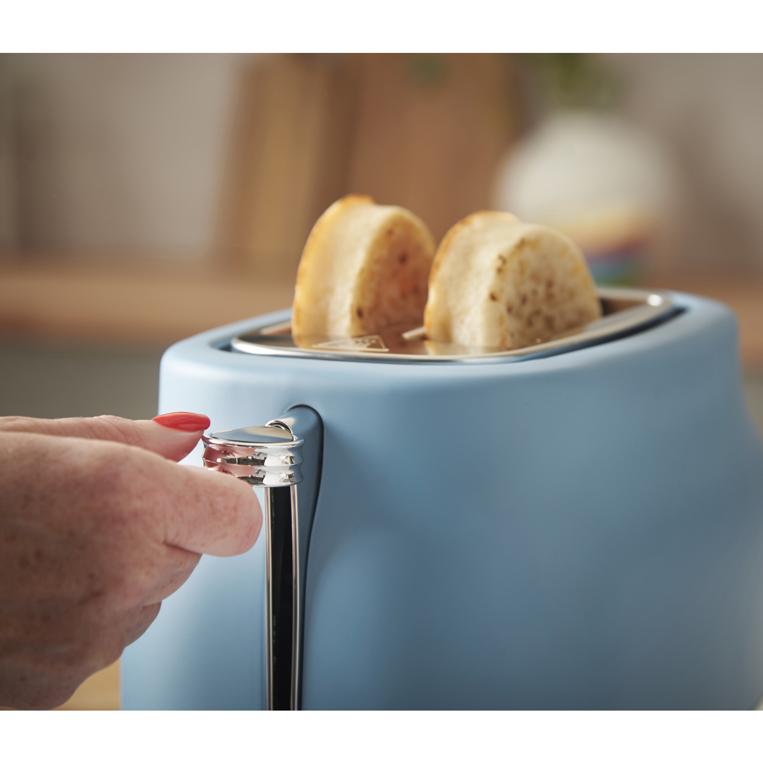 A blue toaster with two slices of toast. A hand presses the lever. The background is blurred.