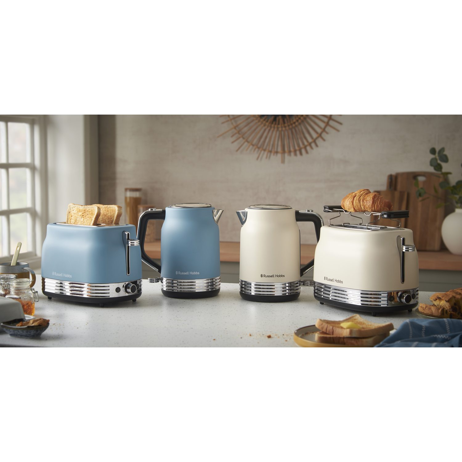 A kitchen scene with two toasters, two kettles, and toast. The toasters are blue and cream, the kettles blue and cream, on a counter.