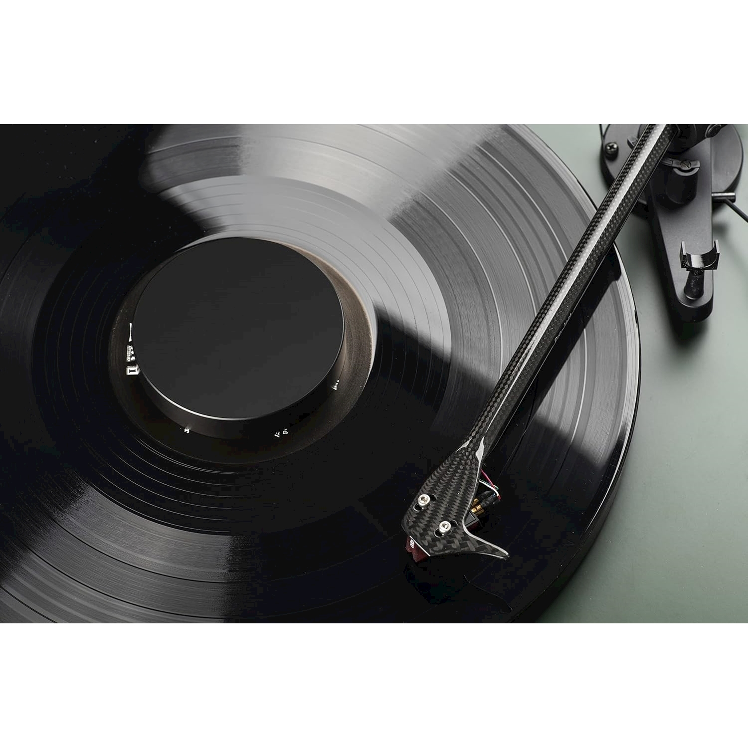 Un disco in vinile nero su un giradischi. La puntina è sul disco. Lo sfondo è una superficie verde chiaro.