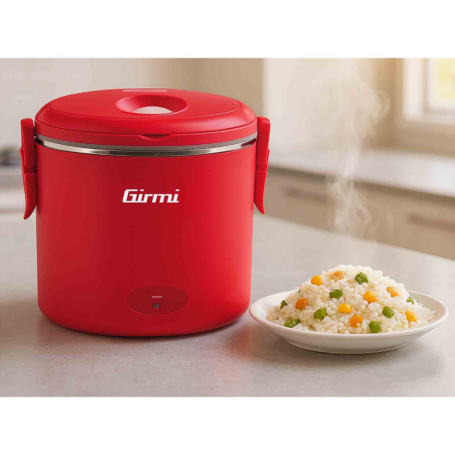Cuociriso Girmi rosso accanto a un piatto di riso con piselli e mais. Il vapore sale. Lo sfondo mostra una cucina.