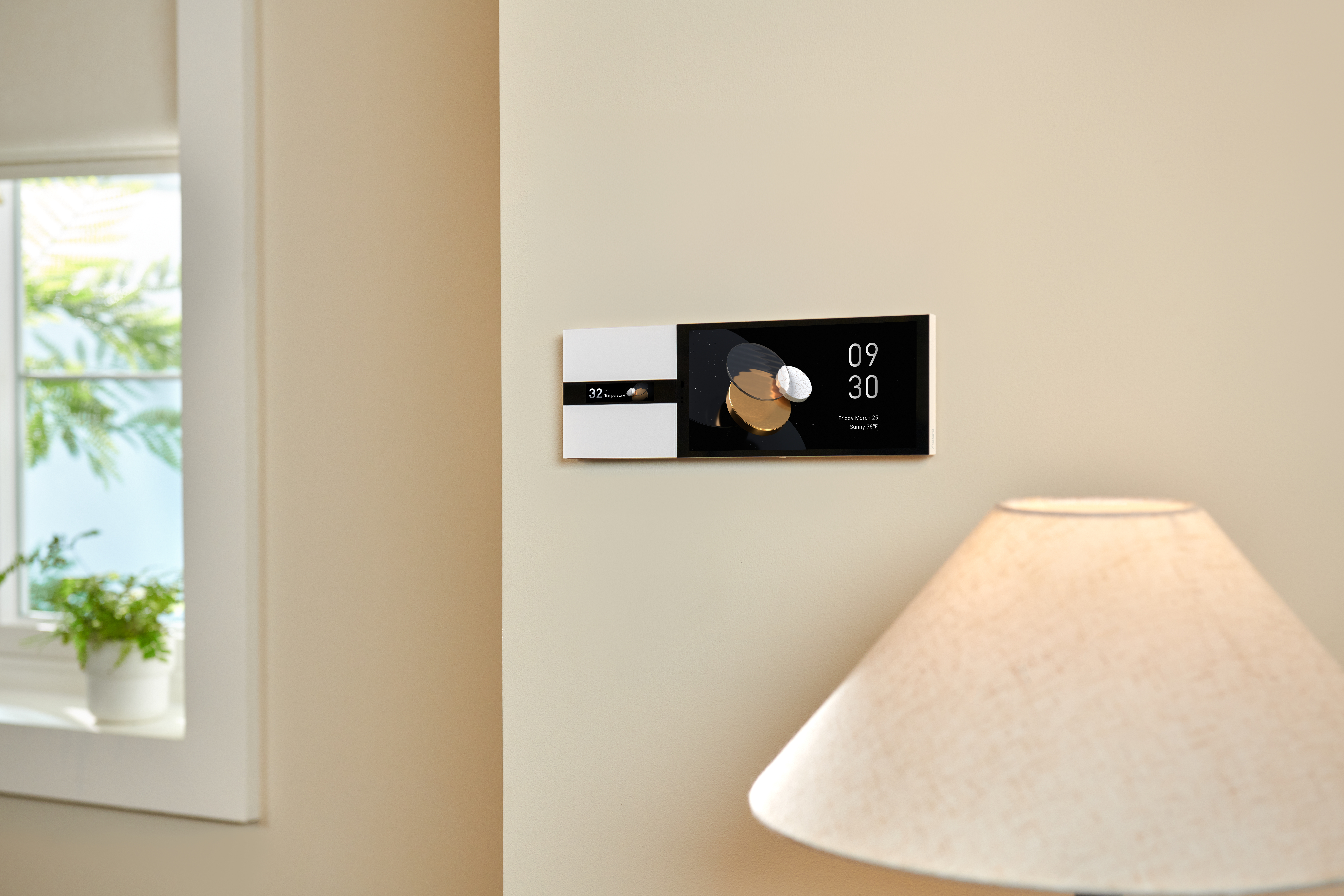Ein an der Wand befestigtes Smart-Display zeigt Zeit, Datum und Wetter. Eine Lampe und ein Fenster befinden sich im Vordergrund. Neutralfarbene Wände.