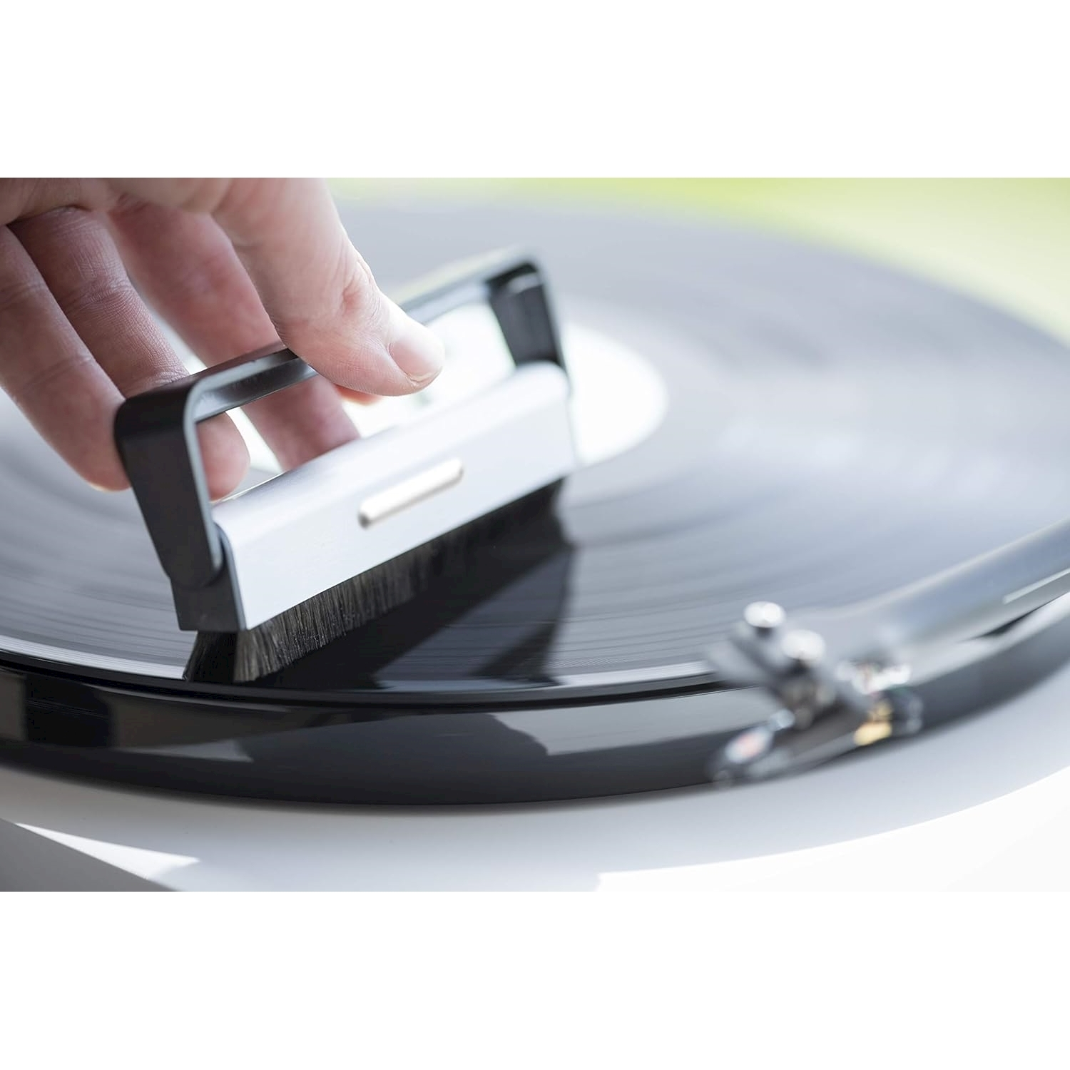 Una mano tiene una spazzola per la pulizia sopra un disco in vinile nero. La spazzola sta pulendo il disco. Il giradischi è sullo sfondo.