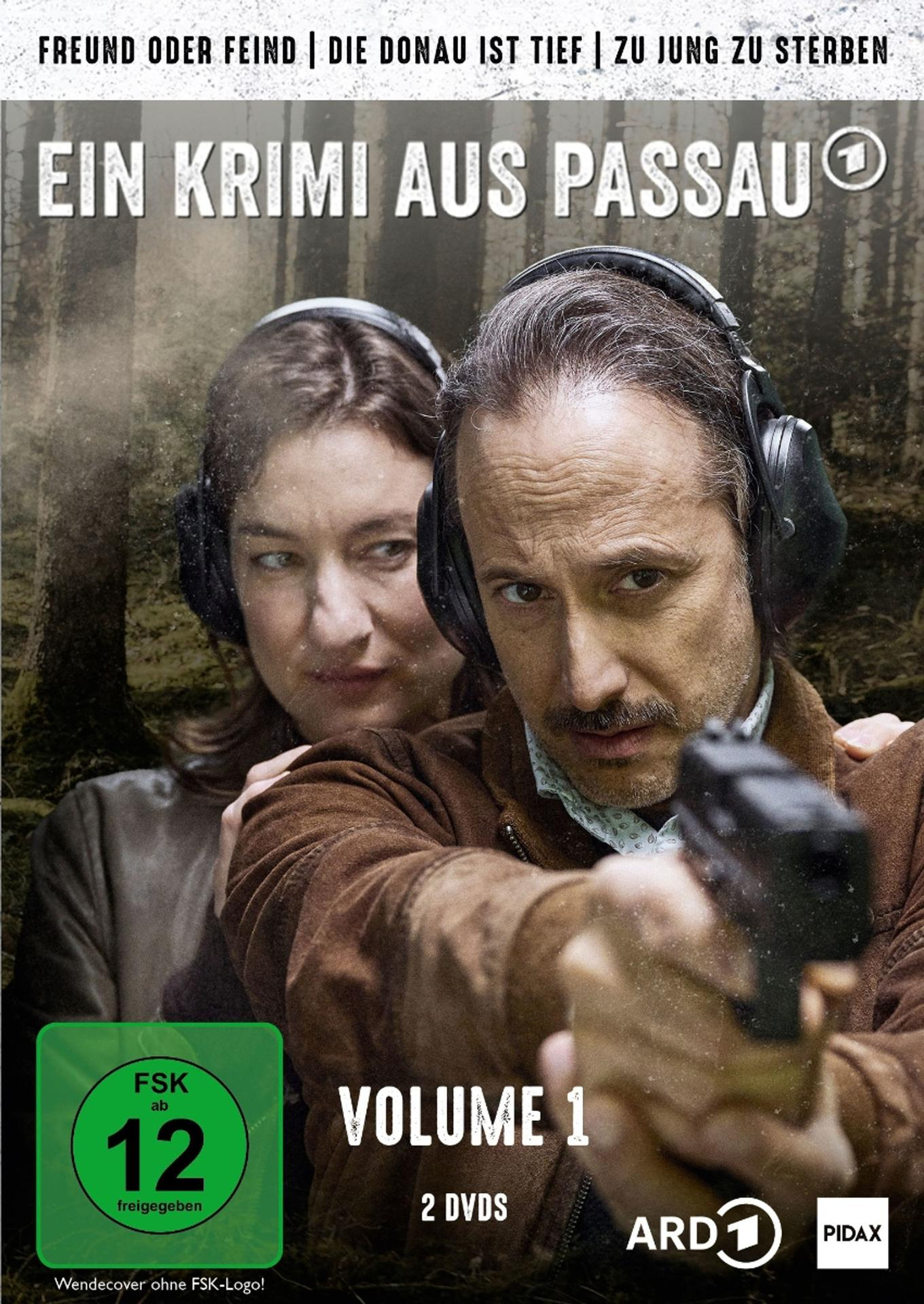 Mann mit Waffe zielt, Frau hinter ihm, Wald im Hintergrund.