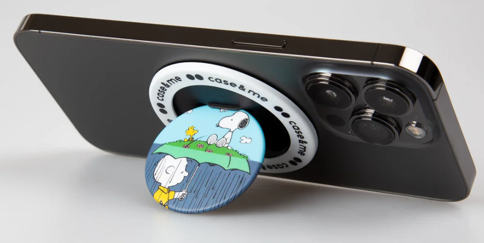 Schwarzes iPhone mit Snoopy-Handyhalterung. Der Griff zeigt Charlie Brown unter einem Regenschirm und Snoopy mit Woodstock.