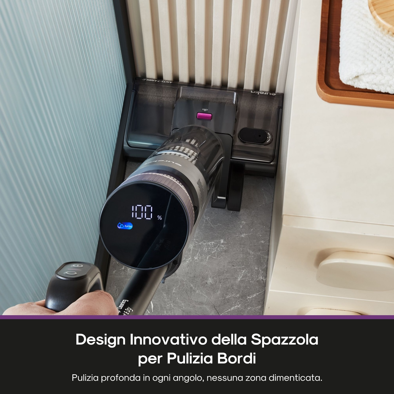 Un aspirapolvere nero e grigio con display digitale sta pulendo un muro. Il display mostra 100%. Una mano tiene l'impugnatura.