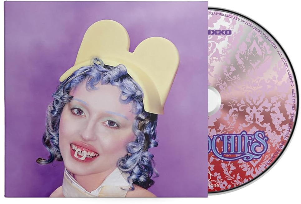 Album borító sárga kalapot és kék hajat viselő személlyel. Egy CD látható jobbra. A személynek fogbűbája van.