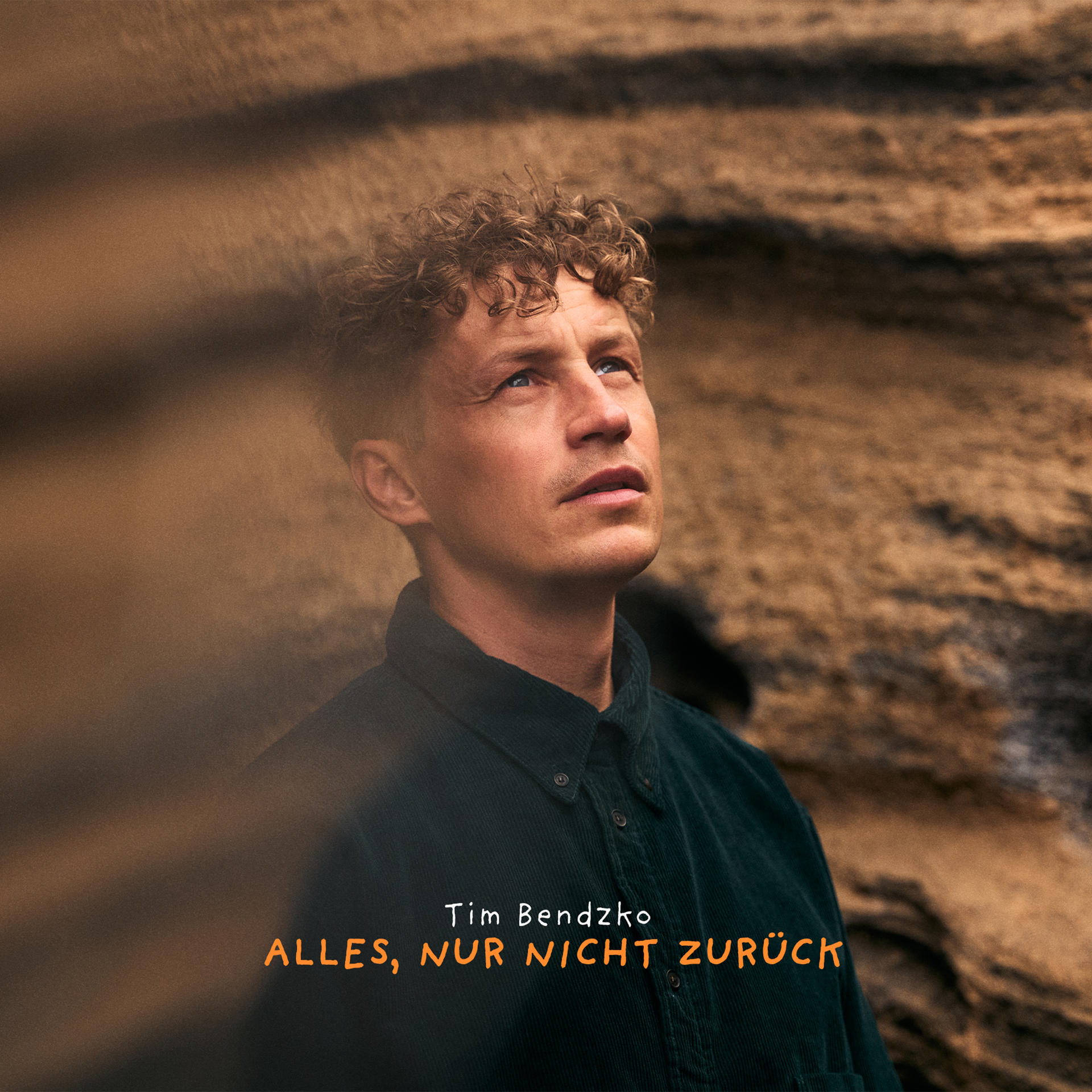 Ein Mann mit lockigem Haar blickt nach oben. Text: Alles, nur nicht zurück.