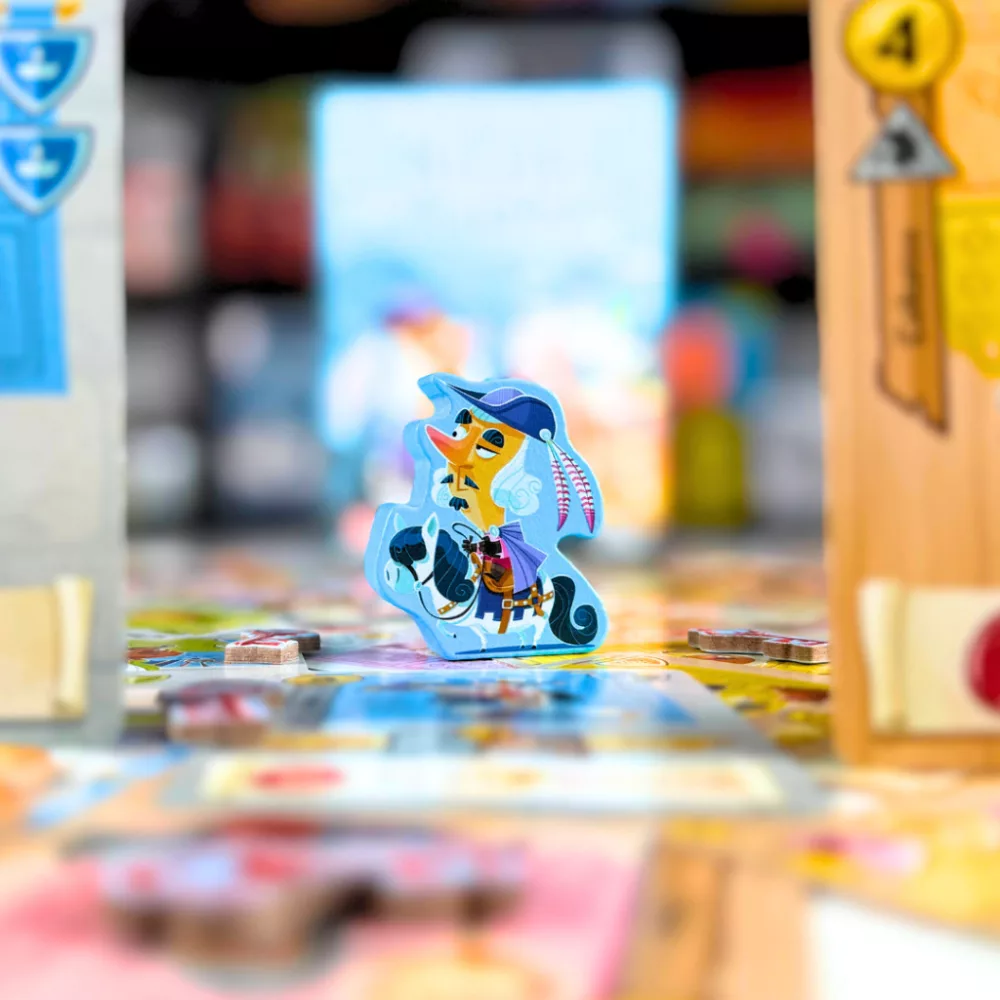 Egy lovagló rajzfilmfigurát ábrázoló játékkocka egy társasjátékban. A karakter kalapot és köpenyt visel. Más játékelemek is láthatók.
