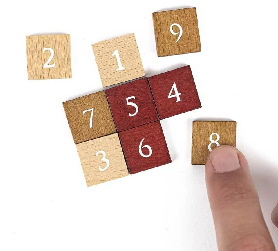 Faszámok 1-9 szétszórtan fehér felületen. Egy ujj érinti a 8-as számú csempét.