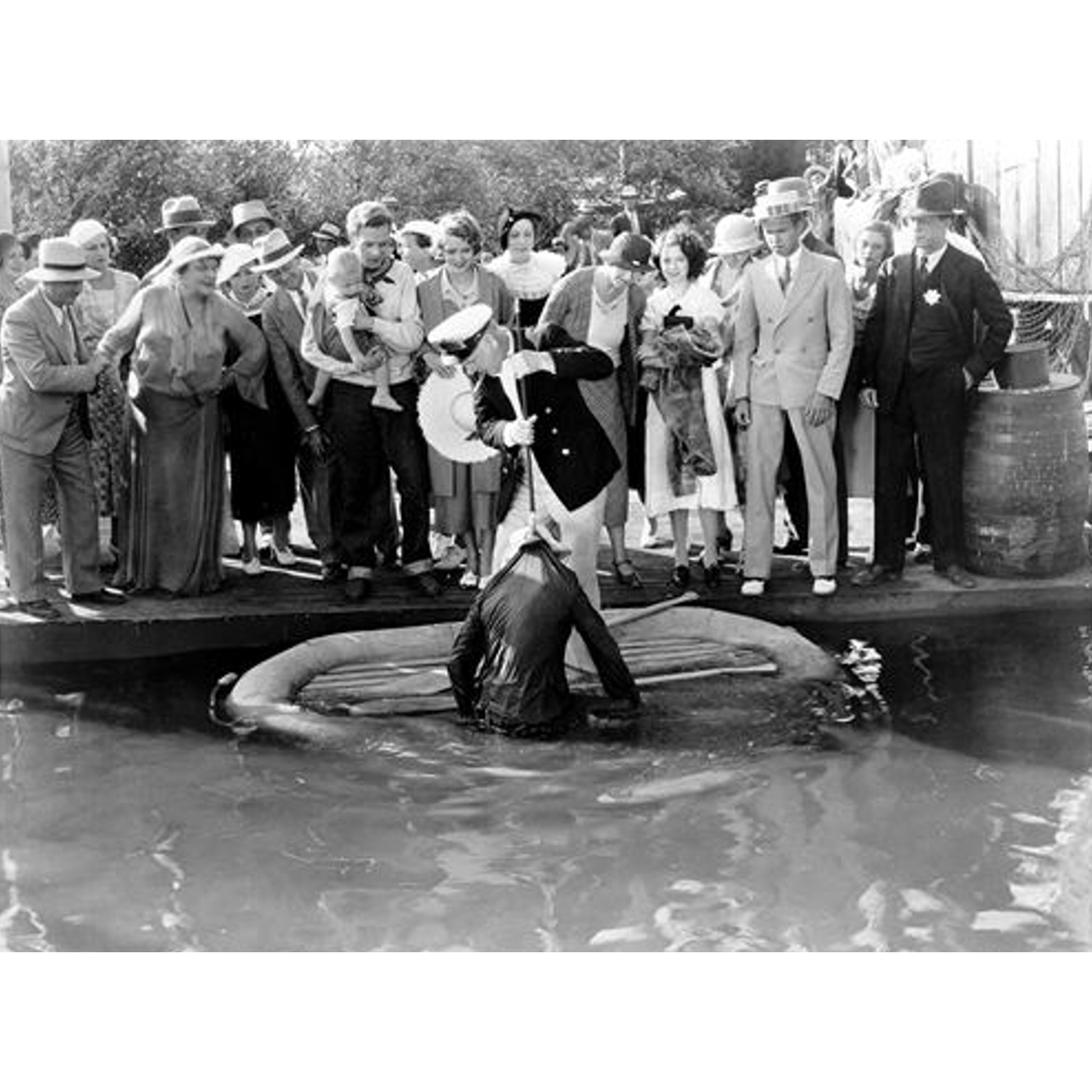 Mensen kijken naar een man in het water. Een man in uniform staat op een pier en wijst. Een kind wordt door een man vastgehouden. Donkere, vintage foto.