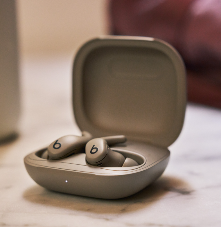 Beats-Ohrhörer in der Ladebox. Das Etui und die Ohrhörer sind hellgrau. Die Ohrhörer zeigen das "b"-Logo. Marmoroberfläche.