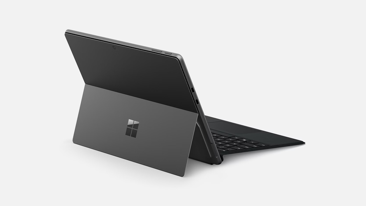 Una tableta Microsoft Surface gris está abierta, mostrando teclado y pantalla. El fondo es blanco.