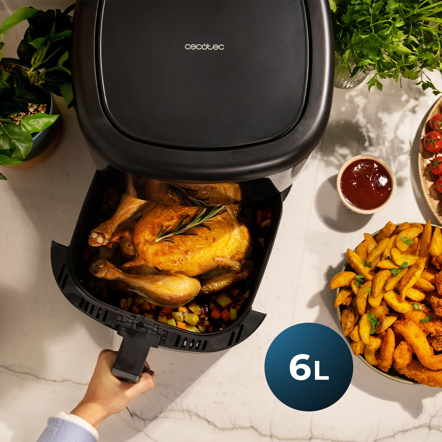 Una friggitrice ad aria nera con un pollo arrosto all'interno, accanto a patatine fritte, ketchup e pomodori. Una mano estrae il cestello. 6L.