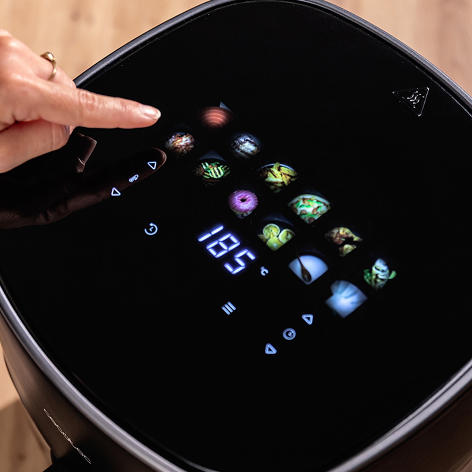 Una mano tocca il pannello di controllo nero di una friggitrice ad aria. Il display mostra 185 gradi, icone di cibo e pulsanti.