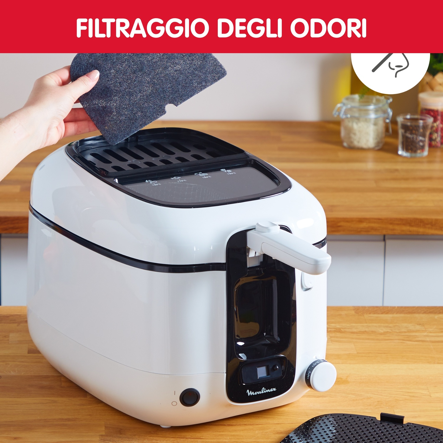 Una persona tiene un filtro sopra una friggitrice bianca. Il testo in alto dice 'Filtrazione odori'. Lo sfondo mostra un piano di lavoro in legno con spezie.