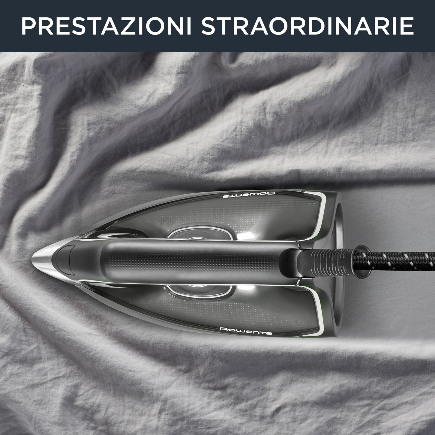 Un ferro da stiro moderno su un lenzuolo grigio. Il ferro è nero e argento con un cavo bianco e nero. Il lenzuolo è stropicciato.