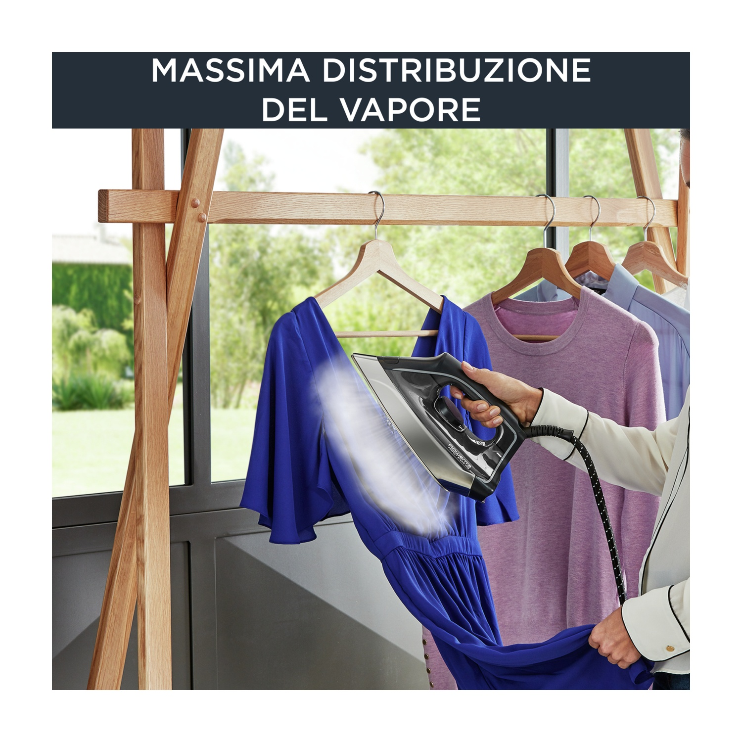 Una persona stira un vestito blu con vapore. I vestiti sono appesi a un appendiabiti in legno. Testo in alto: Massima Distribuzione Del Vapore.