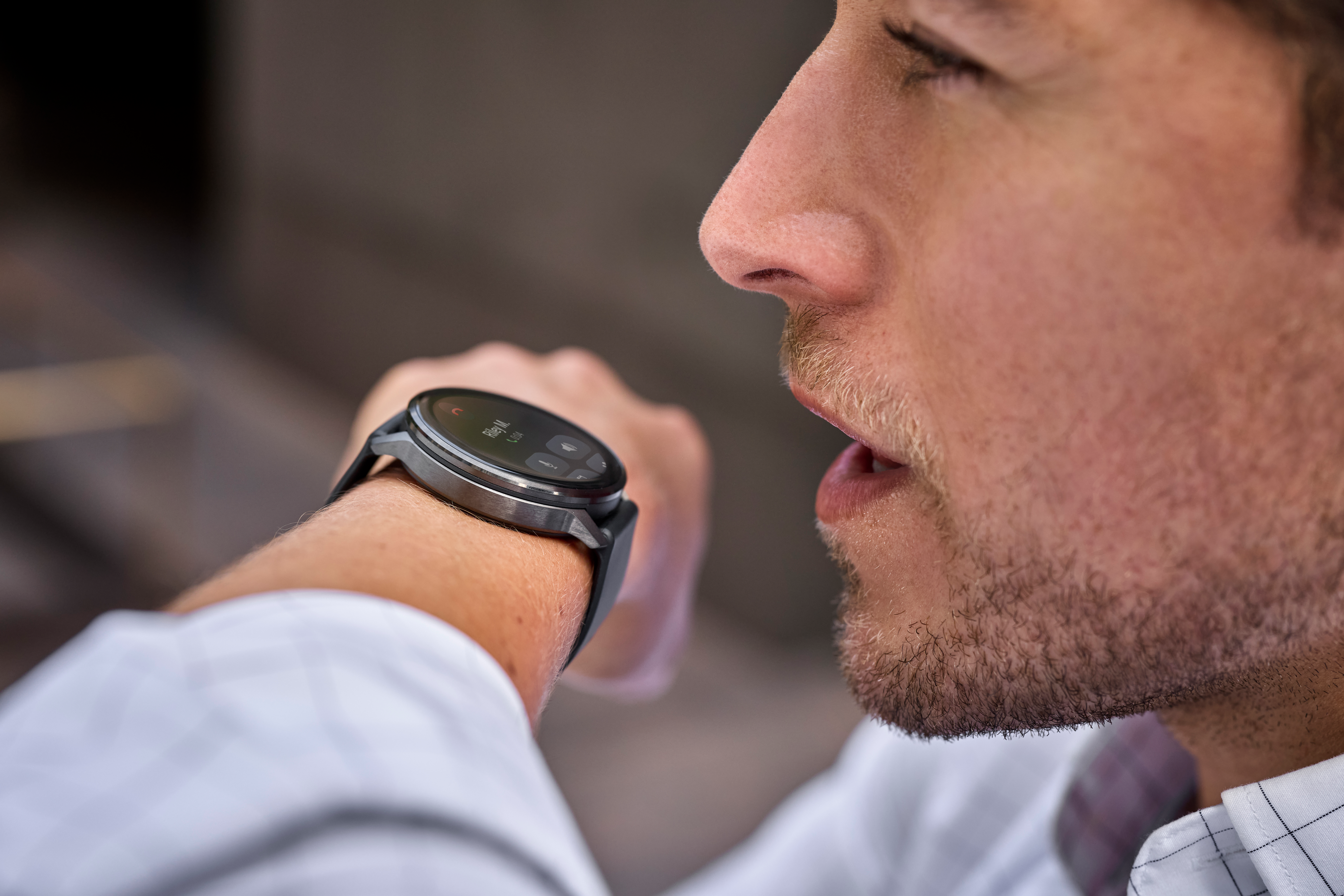 Un uomo guarda uno smartwatch al polso. L'orologio mostra una chiamata da 'Riley M.'.