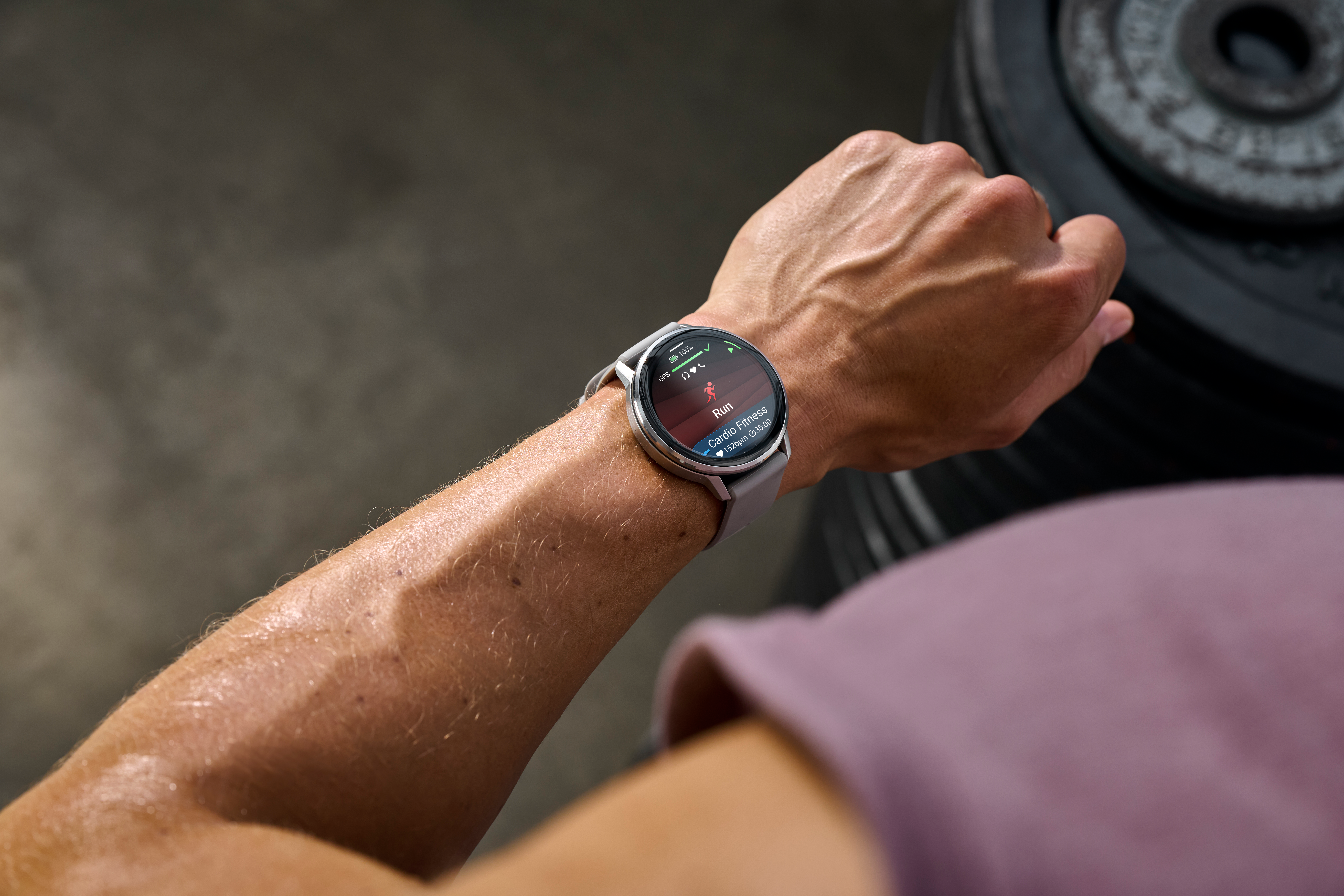 Un bras avec une montre intelligente affichant un entraînement de course. L'arrière-plan comprend des poids. Le bras est en sueur.