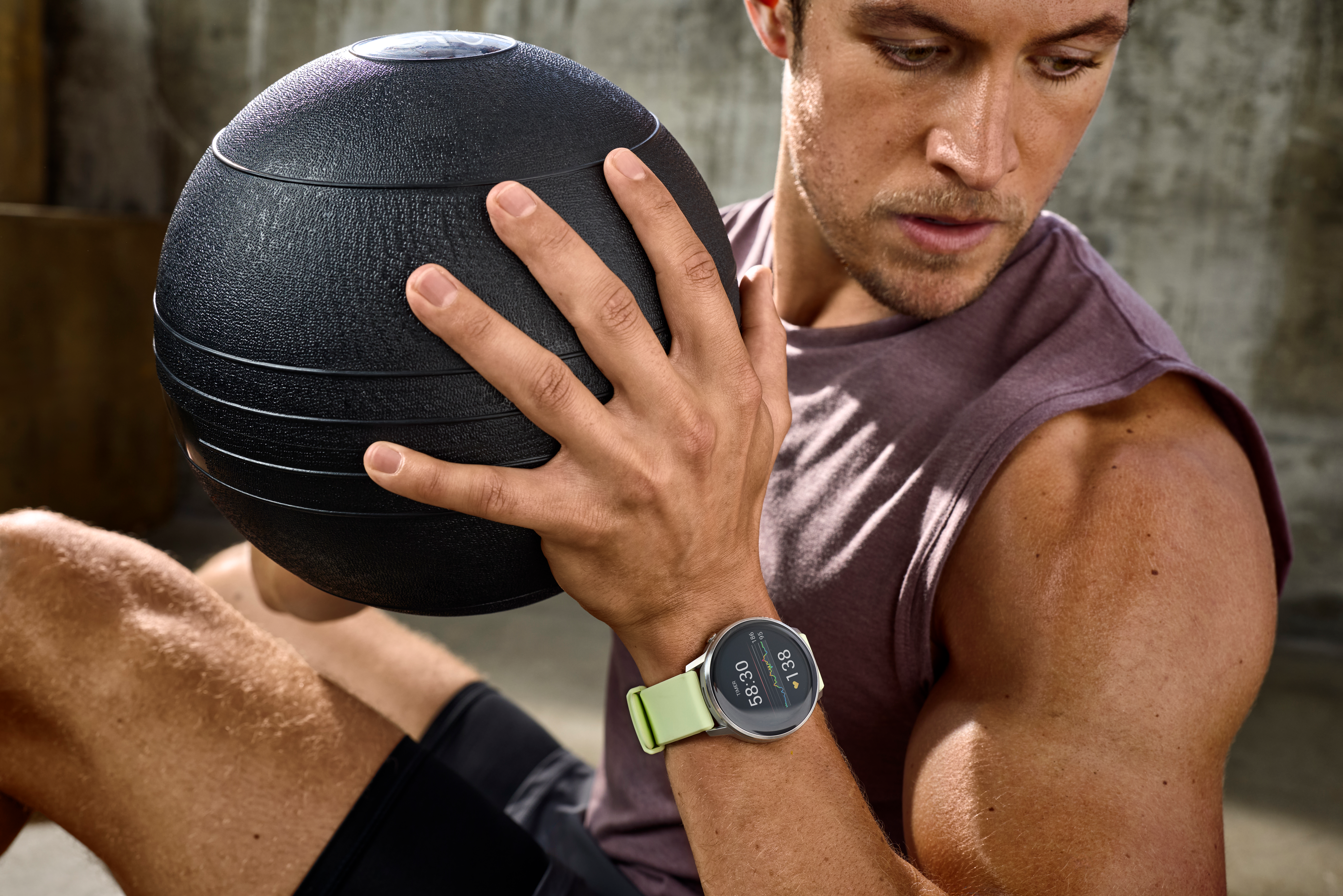 Un homme dans une salle de sport, tenant un ballon médicinal. Il porte une montre. L'accent est mis sur le ballon et le visage de l'homme.