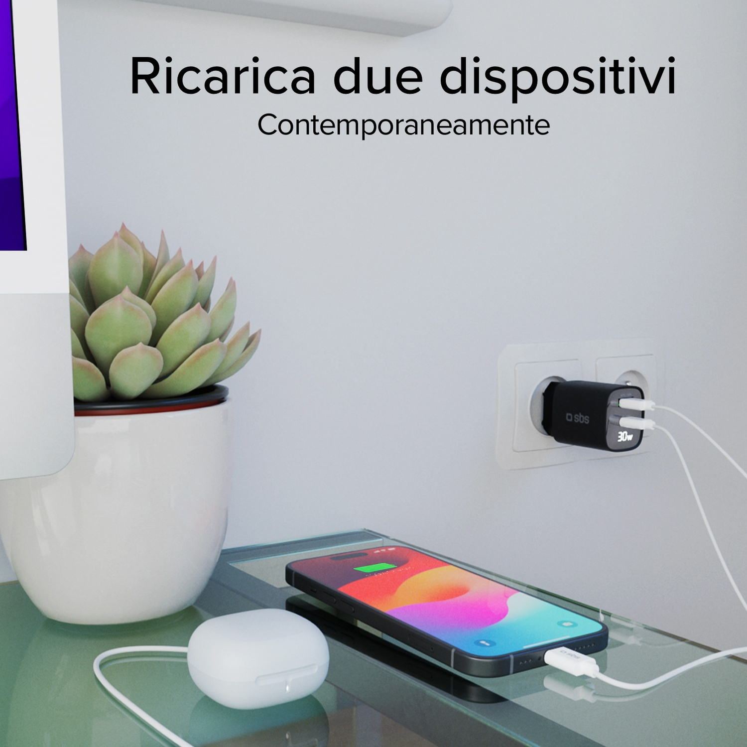 Un telefono, auricolari e caricabatterie sono su un tavolo di vetro. Una pianta è vicina. Il telefono si sta caricando. Una presa a muro è visibile.