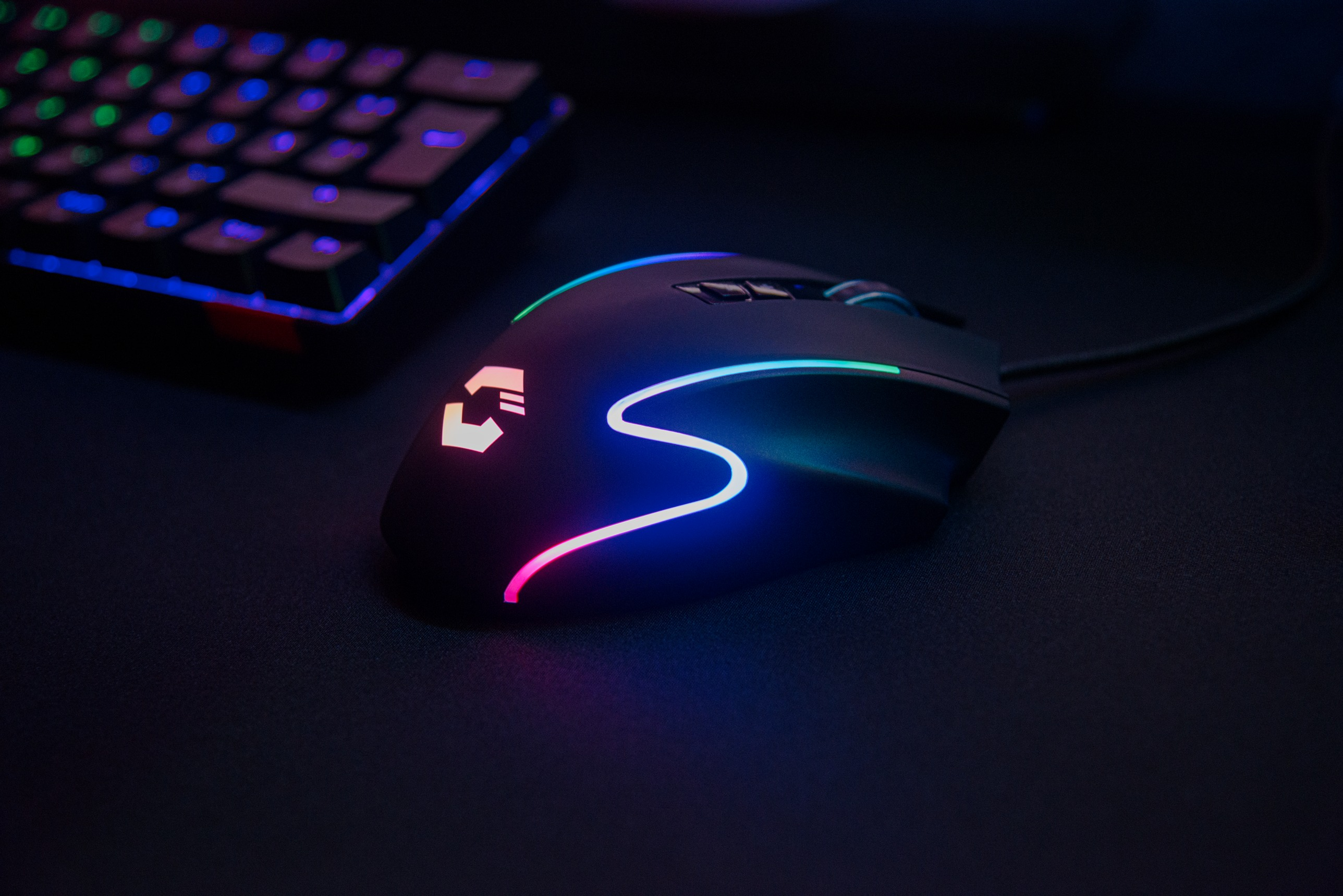 Eine schwarze Gaming-Maus mit RGB-Beleuchtung und eine Tastatur liegen auf einer schwarzen Oberfläche.