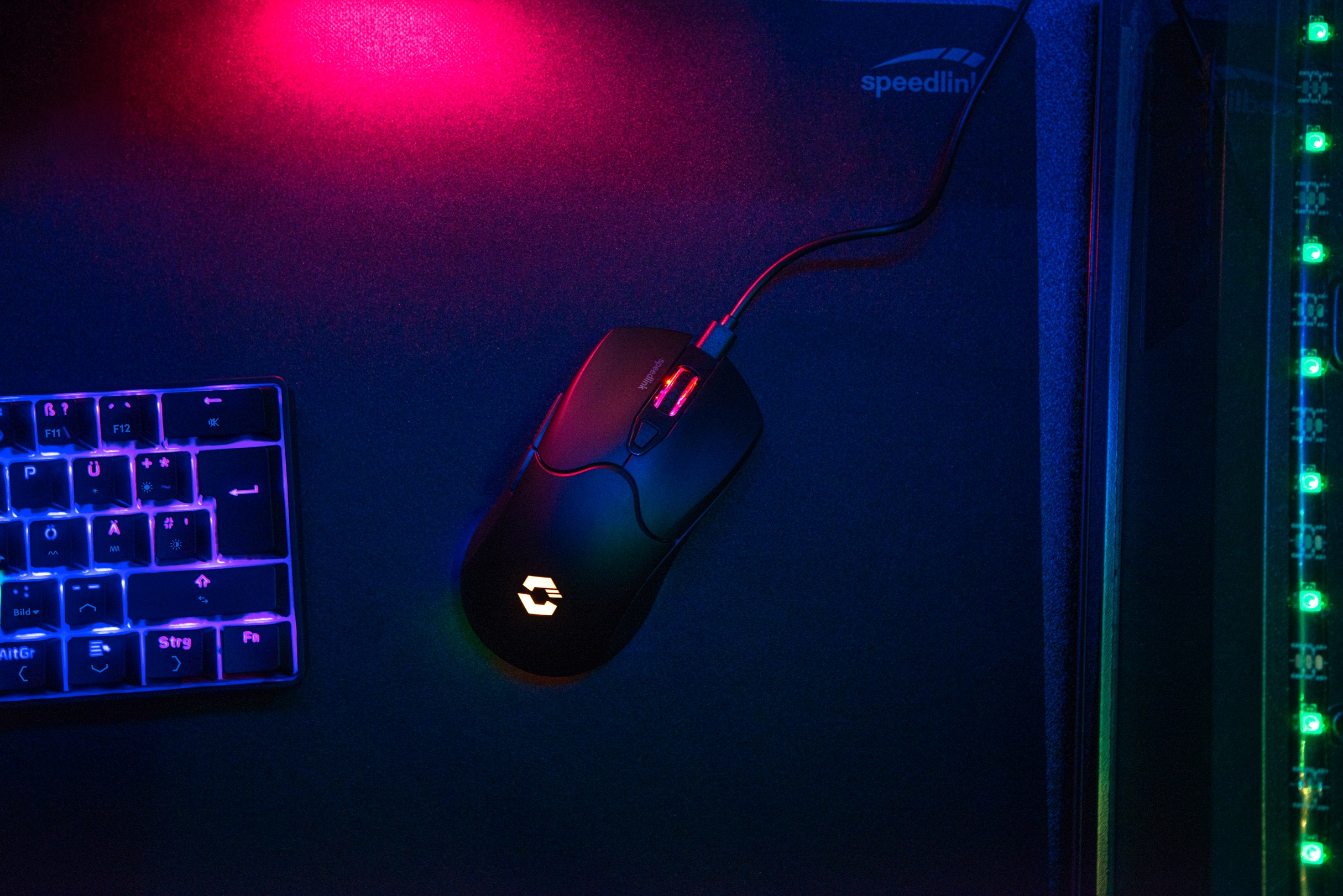 Gaming-Setup mit Tastatur, Maus und RGB-Beleuchtung. Die Maus ist schwarz und kabelgebunden. Die Tastatur hat blaue Tasten.