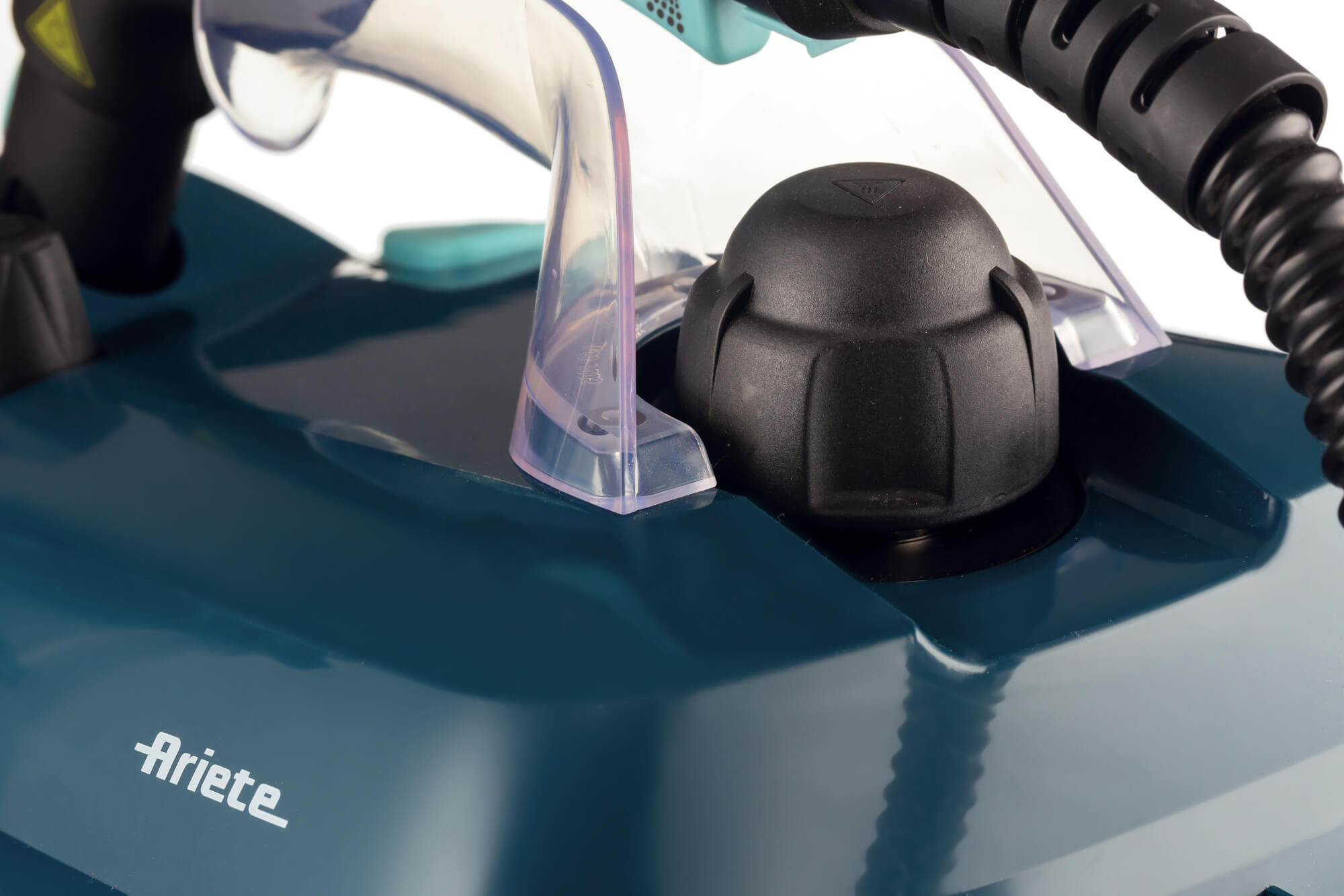 Nahaufnahme eines teal Dampfbügeleisens mit schwarzen Akzenten. Ein schwarzer Knopf und transparente Kunststoffdetails sind sichtbar. Die Marke 'Ariete' ist gedruckt.