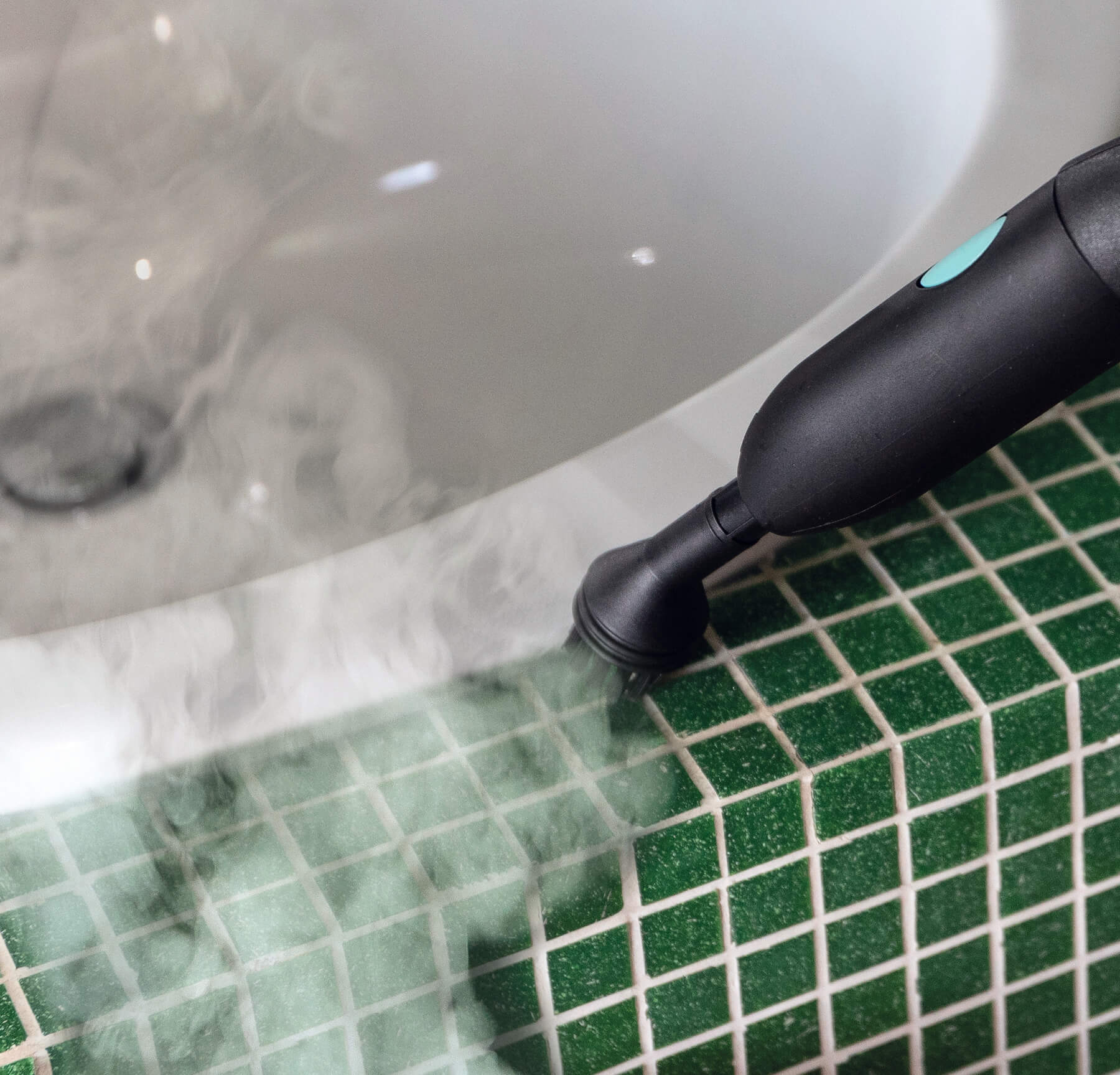 Ein Dampfreiniger reinigt einen grün gefliesten Boden. Dampf steigt um den Rand einer weißen Badewanne auf.