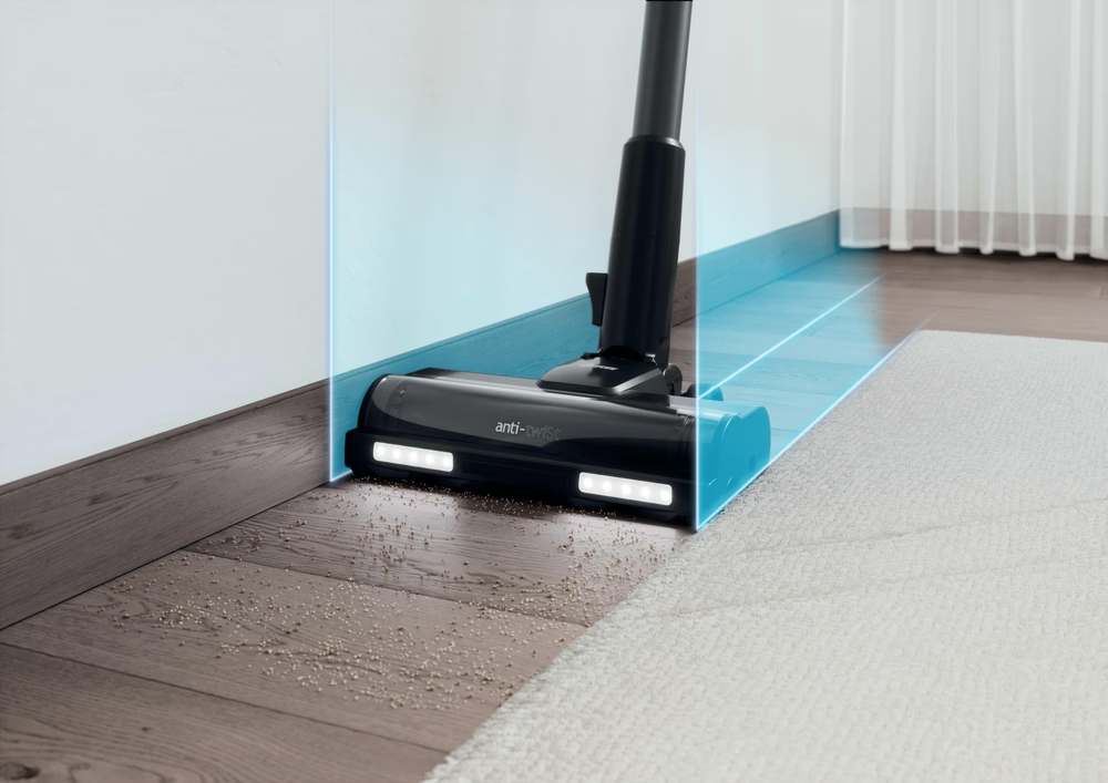 Un aspirapolvere nero pulisce un pavimento in legno e un tappeto. L'aspirapolvere è vicino a un muro con un effetto visivo blu.