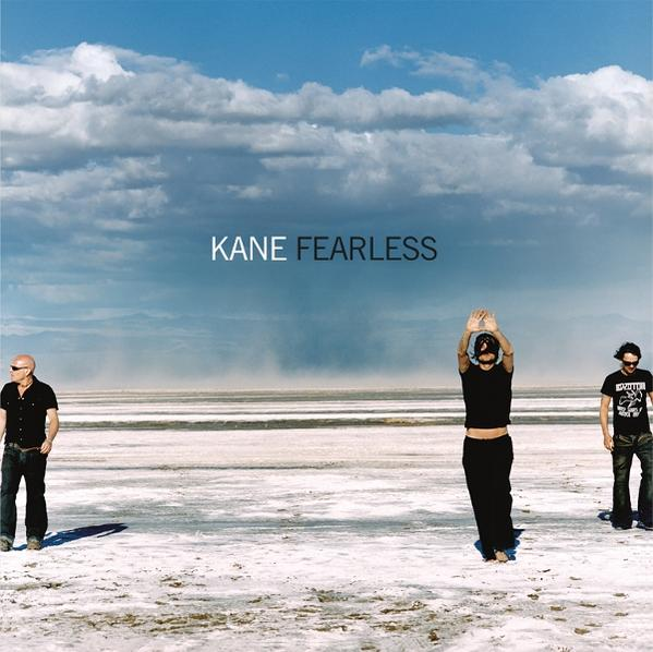 Drei Männer stehen auf einer weißen Ebene unter blauem Himmel. Einer hebt die Hände. Text: KANE FEARLESS.