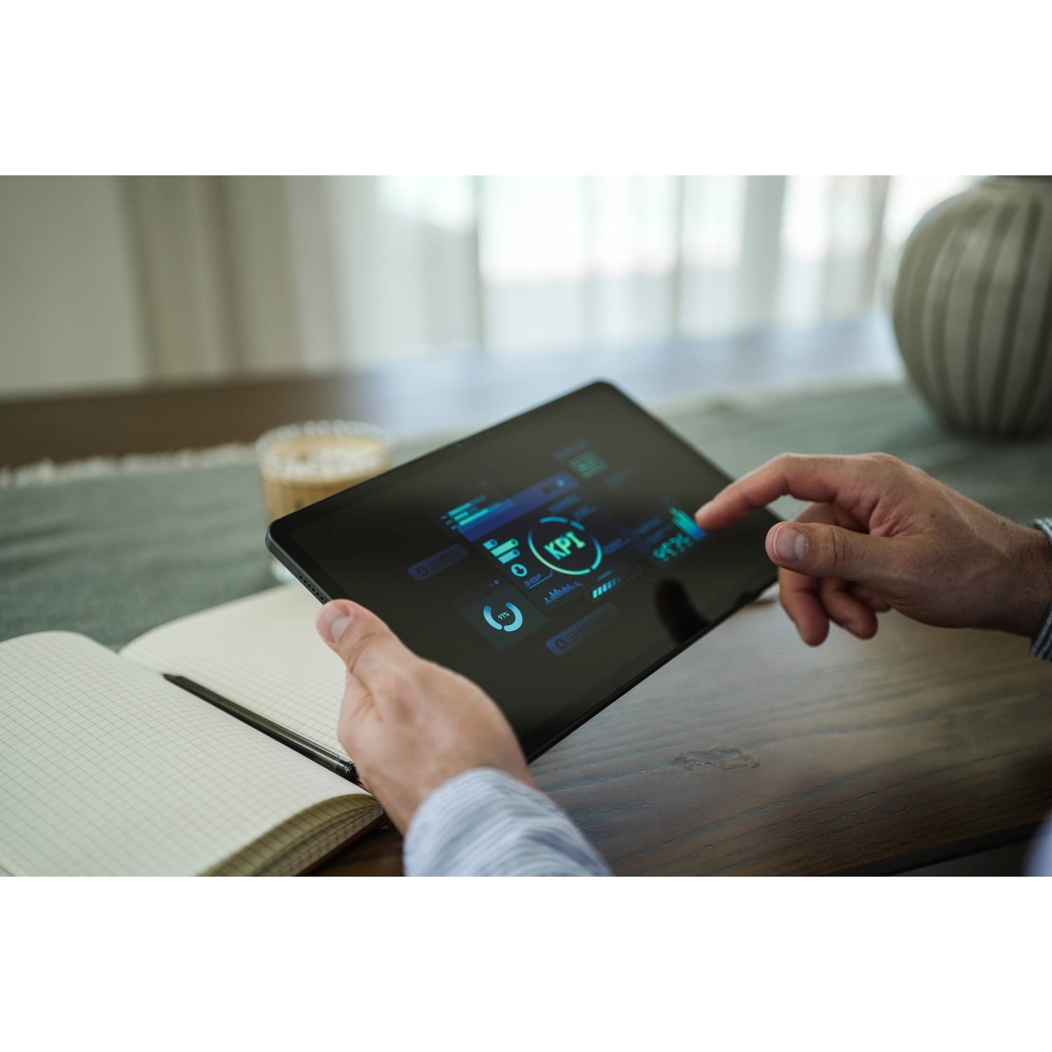 Una persona usa un tablet che mostra un dashboard KPI. Il tablet è su un tavolo di legno, con un taccuino e uno sfondo sfocato.