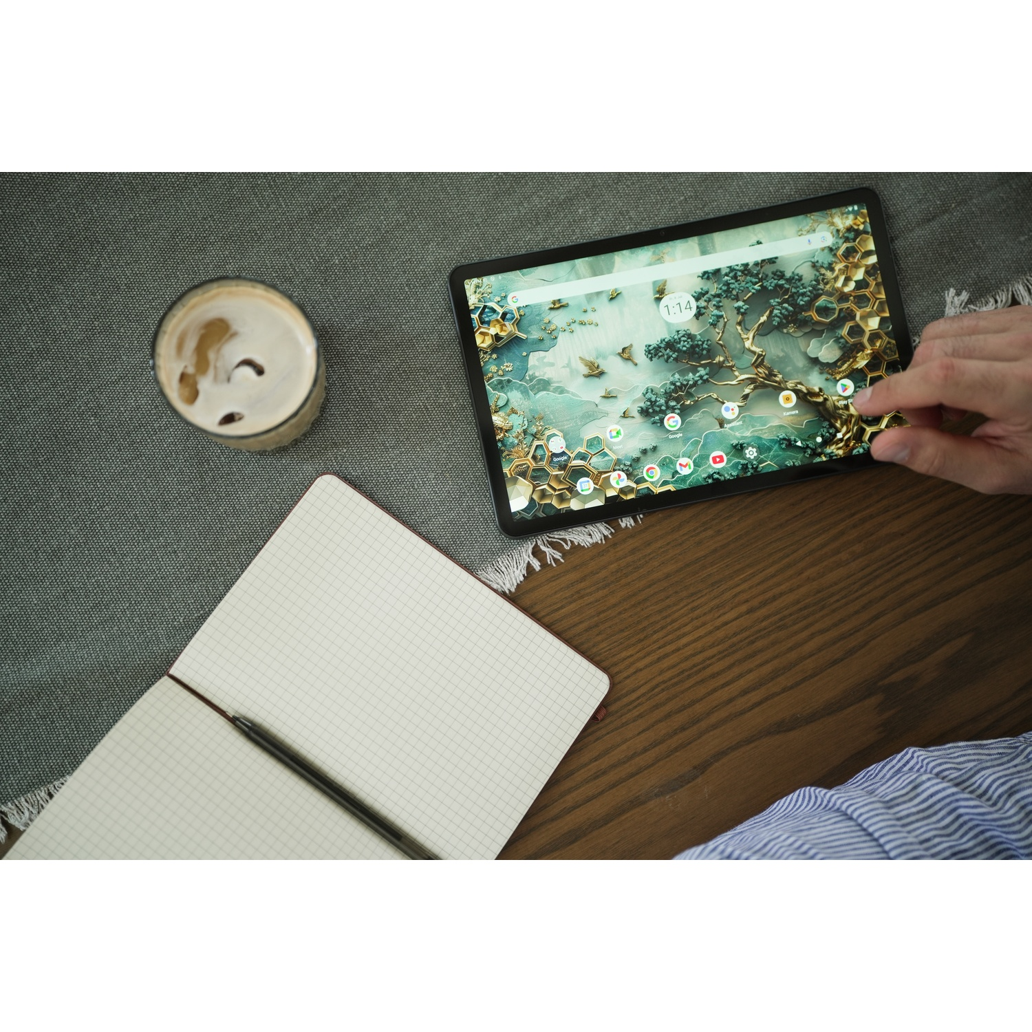 Una persona usa un tablet su un tavolo di legno. Blocco note, caffè e una mano che tocca lo schermo sono visibili. Lo sfondo è artistico.