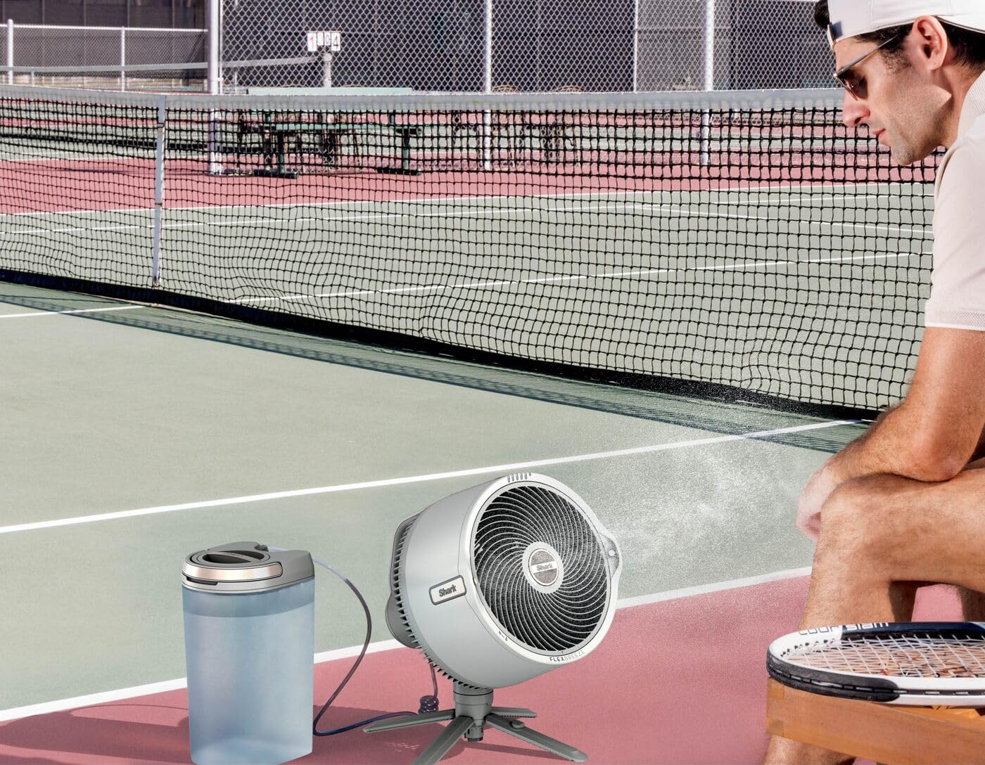 Teniszpálya férfival, ventilátorral és víztartállyal. Férfi napszemüvegben, teniszütővel a széken. Háló a háttérben.