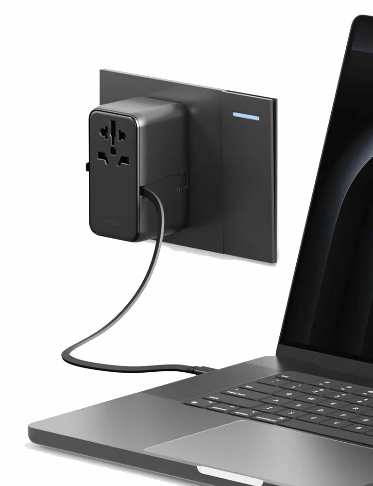 Czarny zasilacz jest podłączony do gniazdka ściennego i połączony z laptopem za pomocą kabla. Laptop jest otwarty.