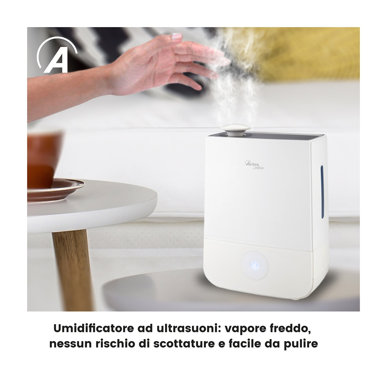 Una mano si protende verso un umidificatore bianco che emette vapore. Una tazza di caffè è su un tavolo. Lo sfondo mostra un letto.