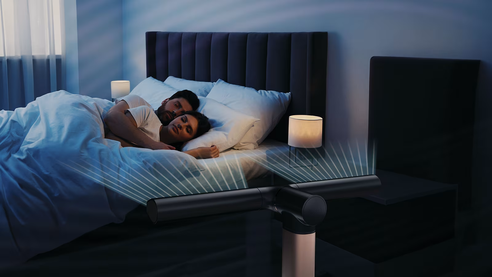 Egy pár alszik az ágyban. A lábnál egy ventilátor van, vonalakat bocsát ki. Lámpák az éjjeliszekrényeken. Sötét színséma.
