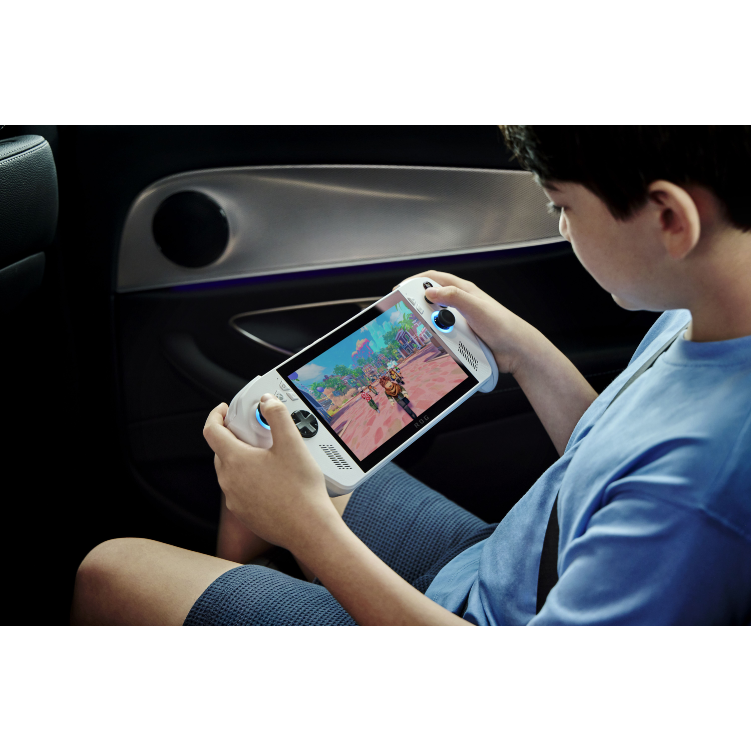 Een kind in een auto speelt met een handheld gaming-apparaat. Het scherm toont een kleurrijk spel. Het kind draagt een blauw shirt en een korte broek.