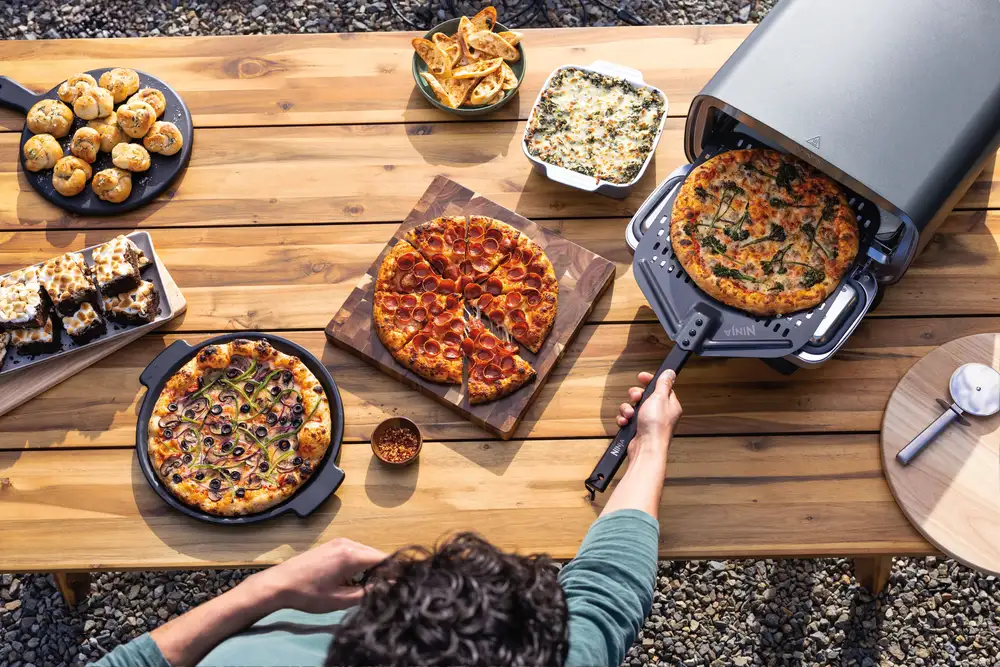 Egy faasztal több pizzával, pékáruval és egy emberrel, aki egy pizzát vesz ki a pultos sütőből.