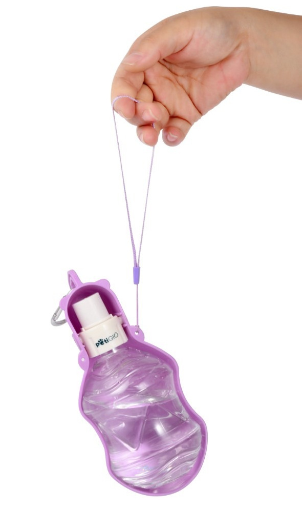 Ręka trzyma fioletową butelkę na wodę dla zwierząt. Butelka jest napełniona wodą i ma białą nasadkę. Tło jest białe.